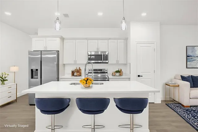 a kitchen with stainless steel appliances granite countertop a sink a stove a refrigerator and white cabinets with wooden floor