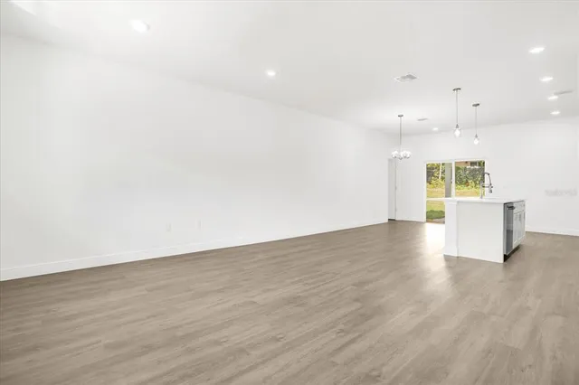 an empty room with wooden floor and kitchen view