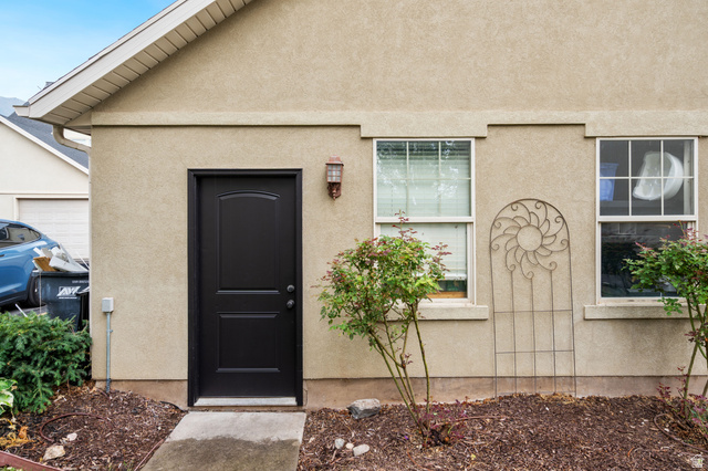 2029 West Crescent Row Mapleton, UT 84664 - Photo 24 of 28 Stucco exterior with a dark-paneled entry door, two double-hung windows, and a decorative metal trellis