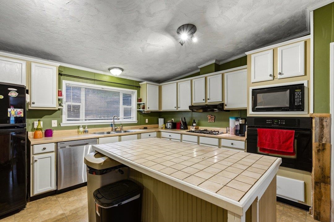 181 EV Road Loris, SC 29569 - Photo 13 of 33 Kitchen with tile countertops, black appliances, ornamental molding, lofted ceiling, and white cabinets