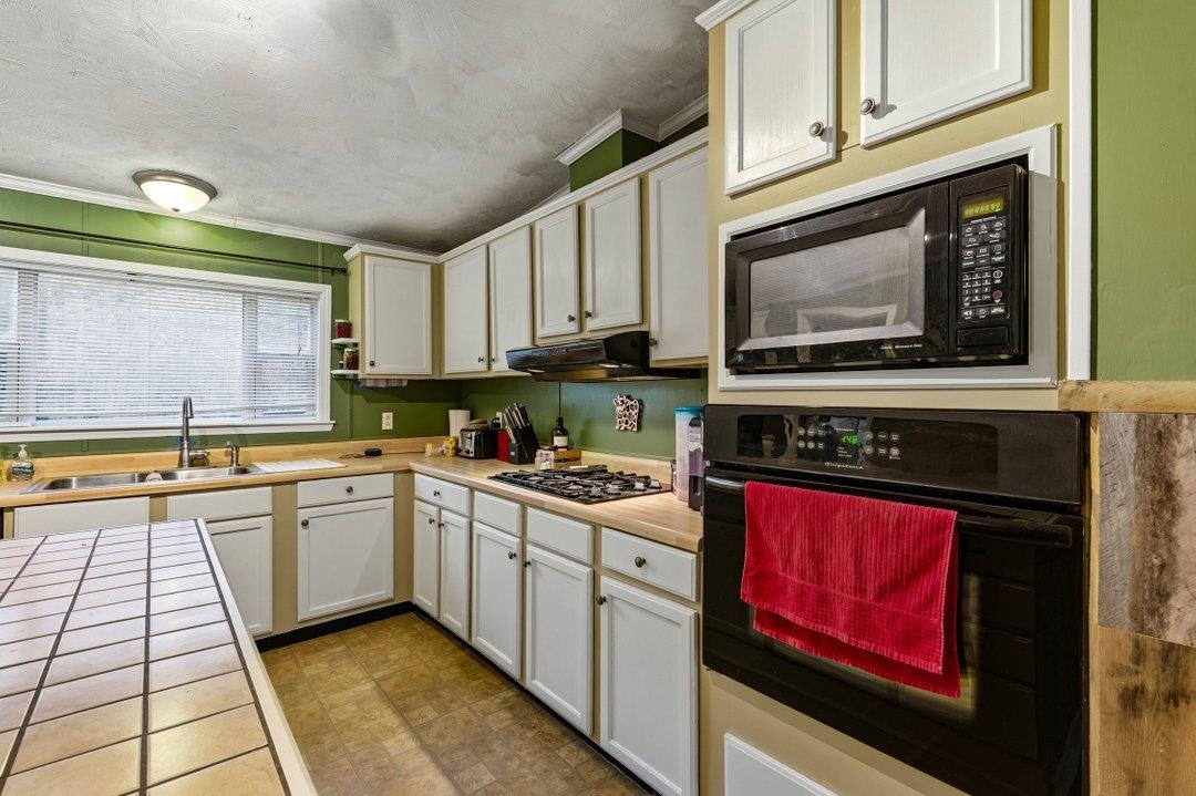 181 EV Road Loris, SC 29569 - Photo 14 of 33 Kitchen featuring black appliances, white cabinets, crown molding, tile countertops, and a textured ceiling