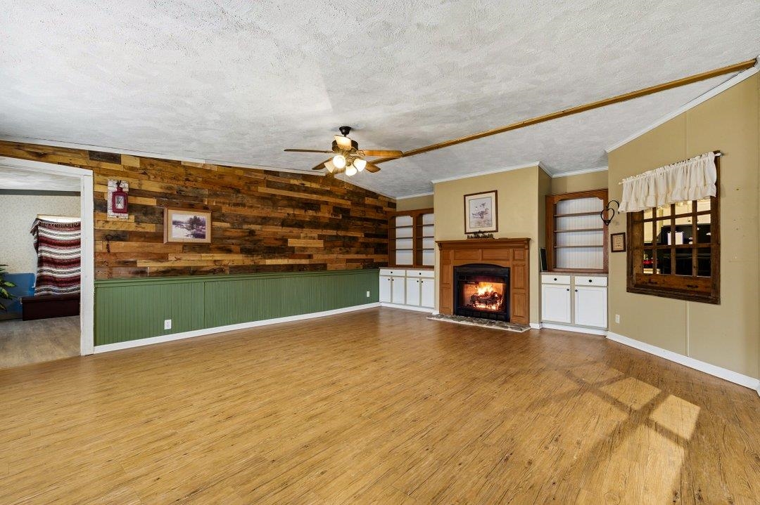 181 EV Road Loris, SC 29569 - Photo 7 of 33 Unfurnished living room featuring wood walls, lofted ceiling, a lit fireplace, a textured ceiling, and light wood-style flooring