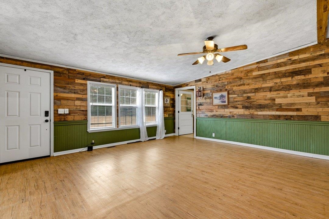 181 EV Road Loris, SC 29569 - Photo 8 of 33 Unfurnished living room with wood walls, a textured ceiling, a ceiling fan, wood finished floors, and wainscoting