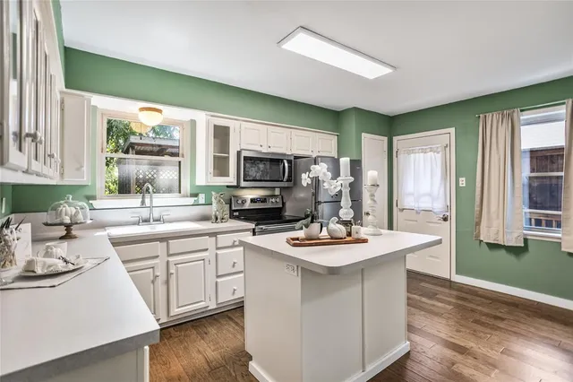 a kitchen with a sink a stove a refrigerator and white cabinets with wooden floor