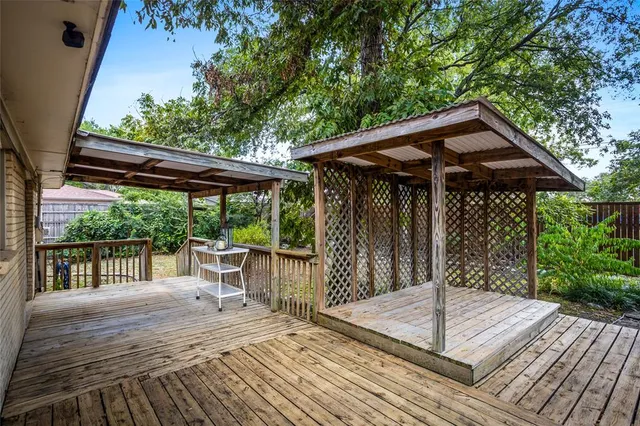 a patio with wooden floor a yard a table and chairs under an umbrella with wooden fence and large trees