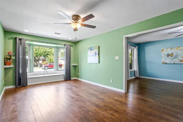 an empty room with wooden floor fan and windows