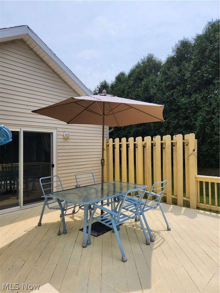 Spacious composite deck featuring a wood-finish surface, substantial yellow privacy fencing, and mature tree backdrop
