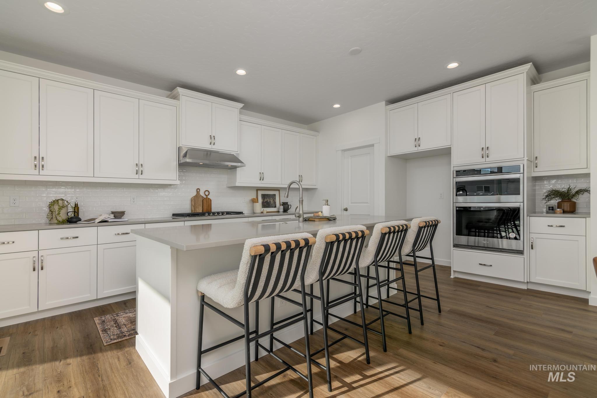 855 West Bay Street Middleton, ID 83644 - Photo 8 of 13 Kitchen with decorative backsplash, a breakfast bar, dark wood finished floors, a kitchen island with sink, and white cabinetry