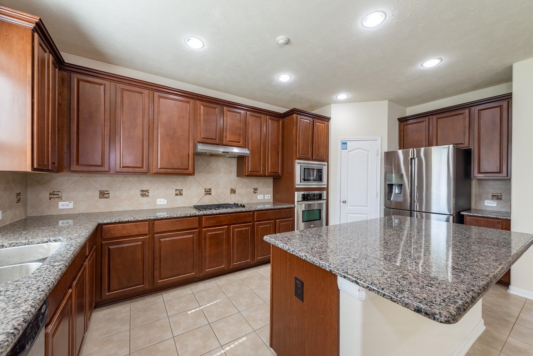 6402 Addlestone Ridge Lane Katy, TX 77494 - Photo 5 of 25 Designed for both everyday living and entertaining, this spacious kitchen features a large granite island, abundant cabinetry, built-in microwave and oven, gas cooktop, and a walk-in pantry conveniently located between the refrigerator and cooking areas for maximum efficiency and storage.