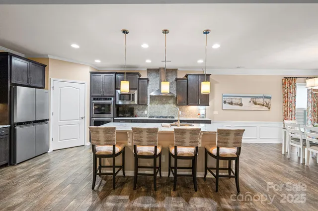 a dining area with stainless steel appliances kitchen island granite countertop a dining table chairs and a refrigerator