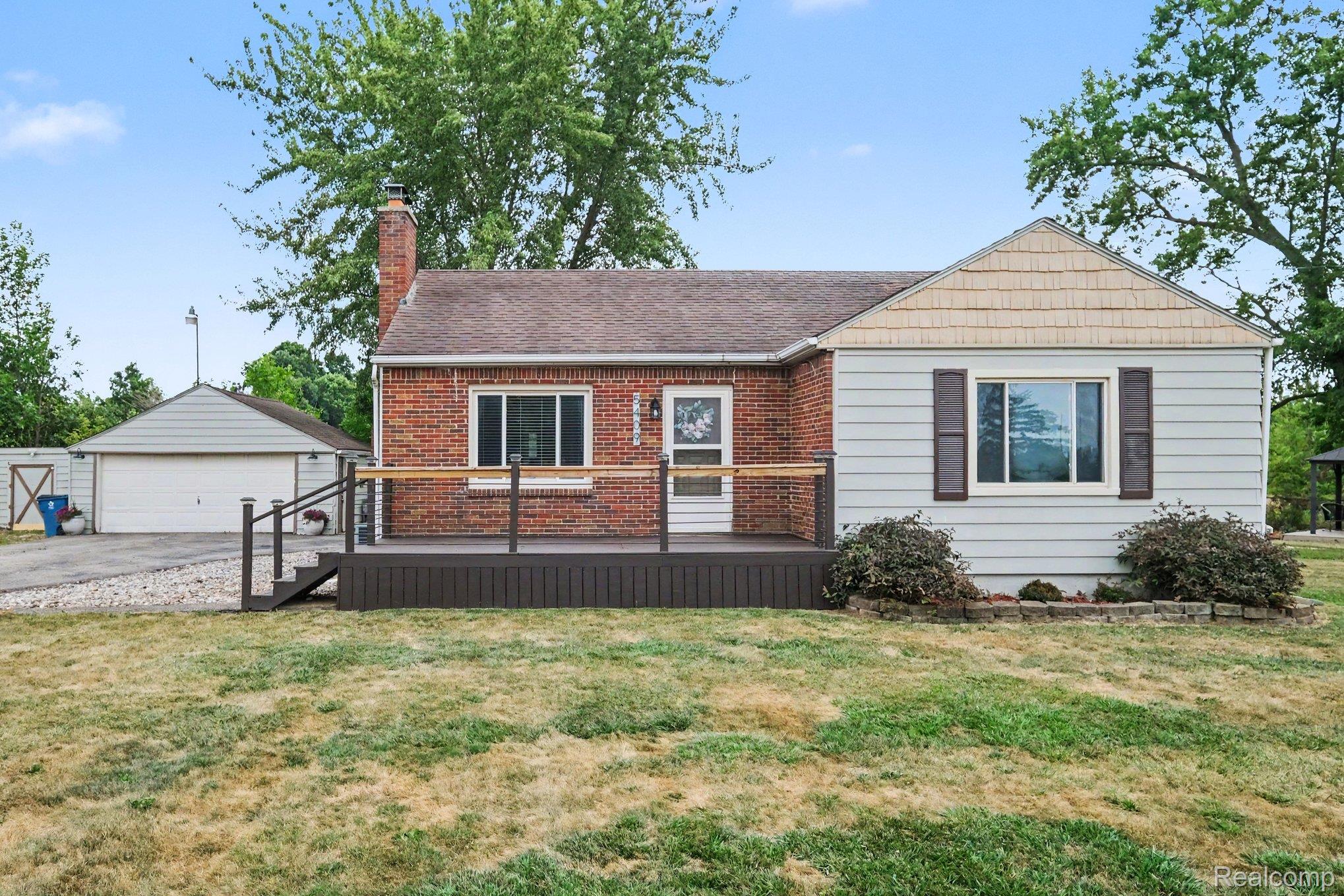 5409 Baldwin Road Swartz Creek, MI 48473 - Photo 1 of 27 Brick and siding exterior featuring a covered deck with railings, a prominent brick chimney, and an attached two-car garage