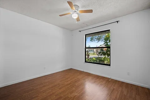 an empty room with wooden floor ceiling fan and windows