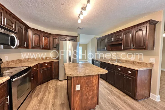 a kitchen with stainless steel appliances granite countertop wooden cabinets a stove top oven a sink and dishwasher a oven with wooden cabinets