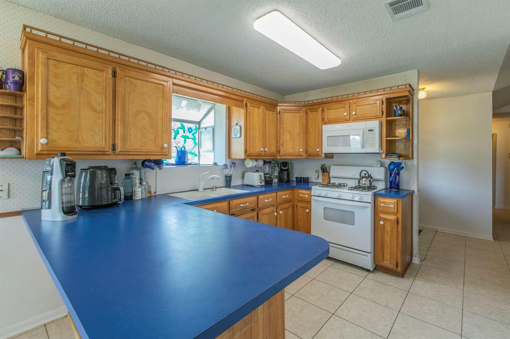 1936 Post Oak Drive Waco, TX 76705 - Photo 7 of 33 Kitchen featuring open shelves, brown cabinets, light tile patterned flooring, white appliances, and dark countertops