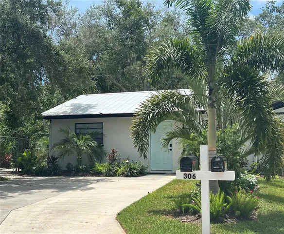 a view of a white house with a small yard plants and large tree