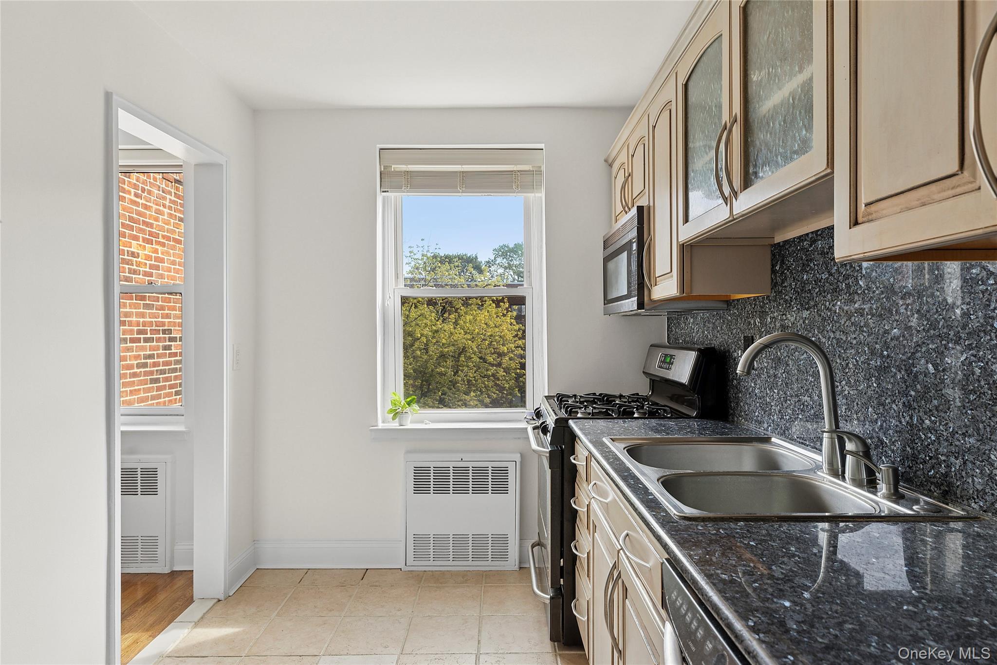 21 Chapel Place, Unit 3M Great Neck, NY 11021 - Photo 7 of 21 Kitchen with stainless steel appliances, glass insert cabinets, light tile patterned floors, tasteful backsplash, and dark stone counters