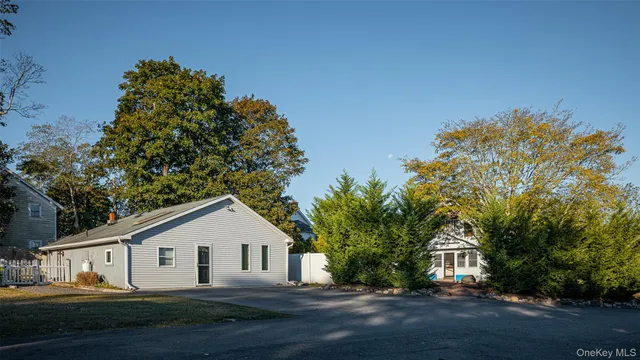 a view of a white house next to a yard with big trees