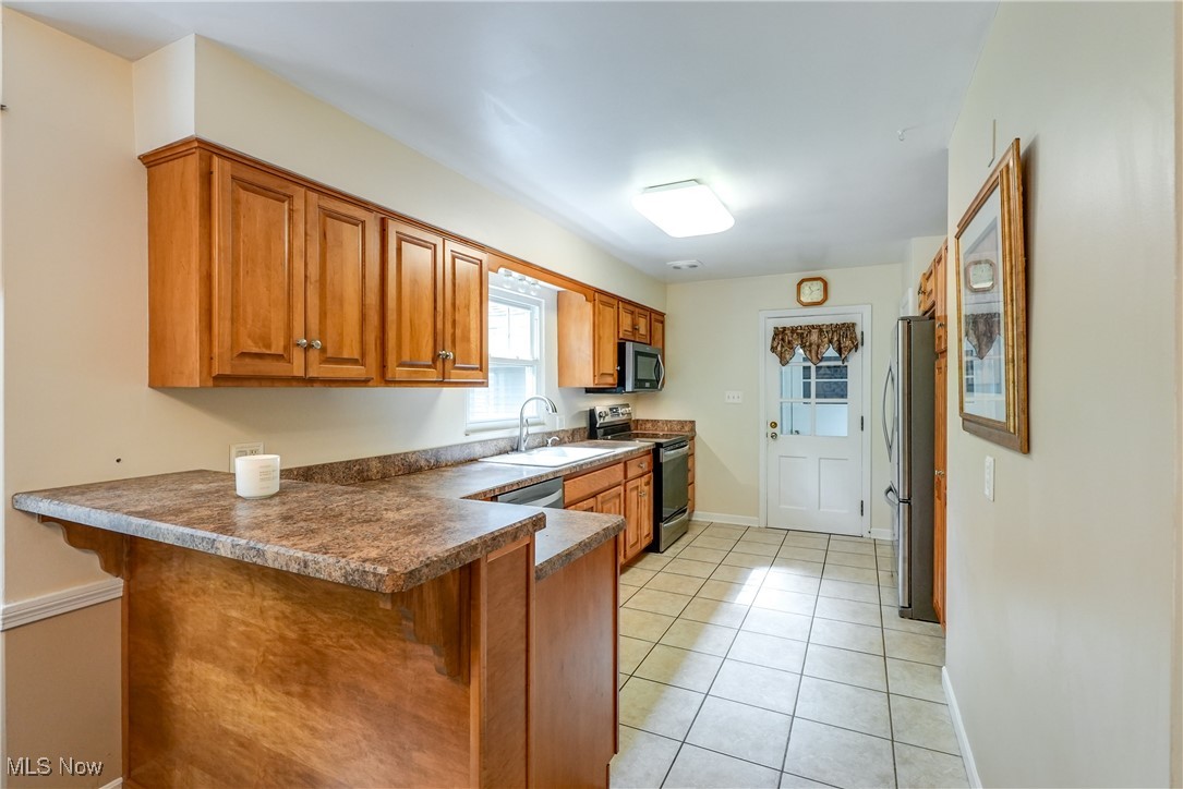 2488 Holgate Road Akron, OH 44313 - Photo 25 of 50 Kitchen featuring light tile patterned floors, appliances with stainless steel finishes (all appliances remain), kitchen peninsula, and sink. Easy access to the breezeway and garage. Great view of the private back yard!