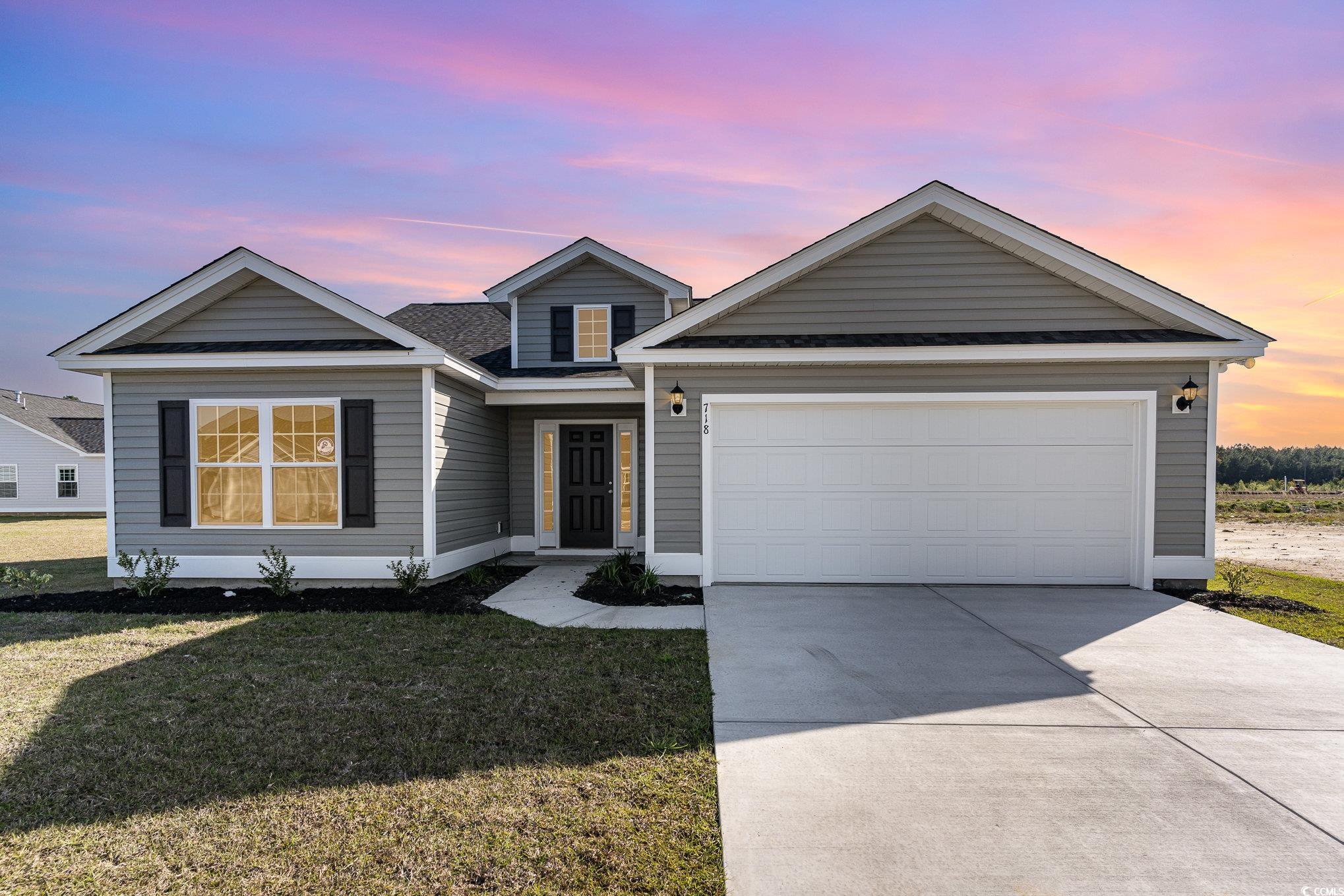 View of front facade featuring concrete driveway, a lawn, an attached garage, and a shingled roof