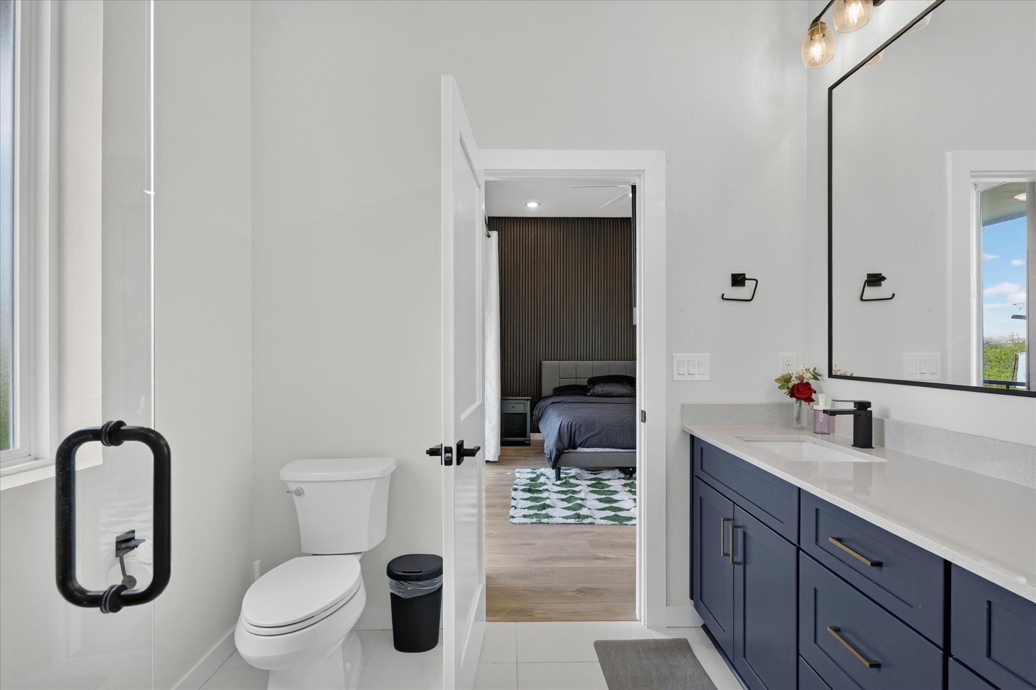 2000 Riverside Farms Road, Unit 8101 Austin, TX 78741 - Photo 24 of 41 This photo showcases a modern bathroom with a sleek design, featuring a large mirror, dual sinks with navy cabinets, and a view into a connected bedroom. Natural light filters through a window, enhancing the bright and clean atmosphere.