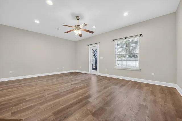 an empty room with wooden floor chandelier fan and windows