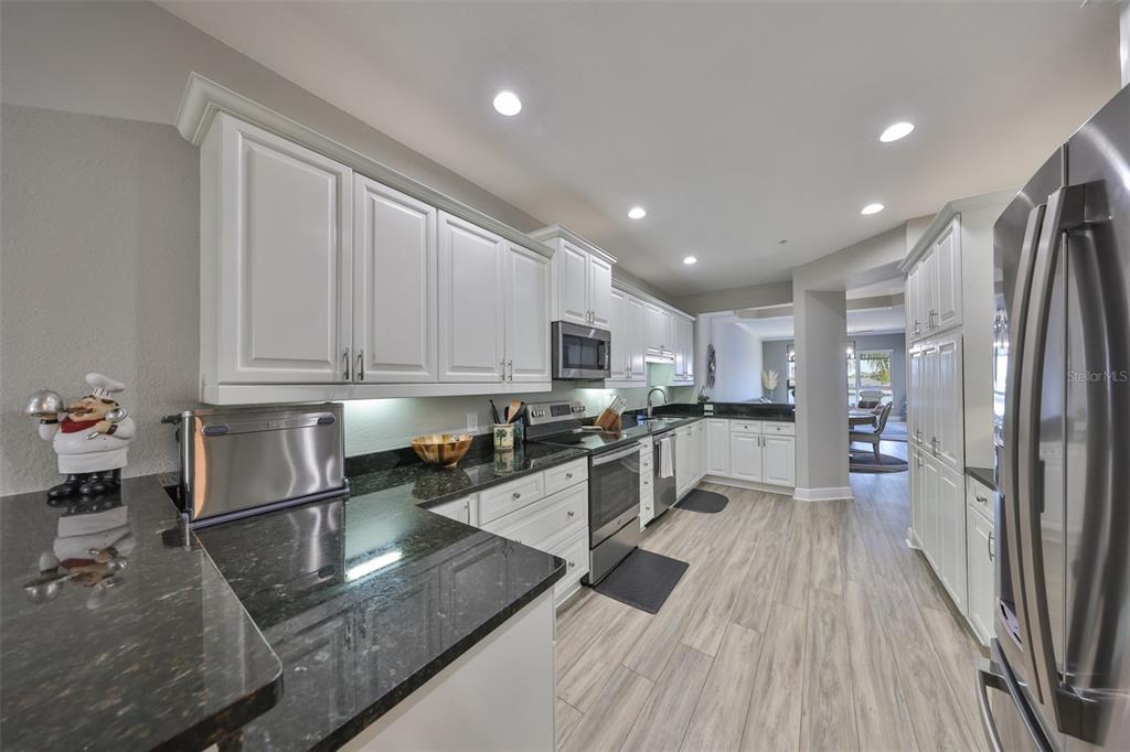 1038 Bellasol Way, Unit 202 Apollo Beach, FL 33572 - Photo 7 of 52 a kitchen with stainless steel appliances granite countertop a refrigerator a sink dishwasher a stove and white countertops with wooden floor