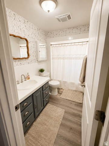 303 North Main Street Grace, ID 83241 - Photo 15 of 22 Full bathroom featuring a single vanity with a white countertop and dark gray cabinetry, wood-finish flooring, a white tiled shower surround, and patterned wallpaper