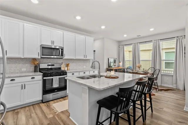 a open kitchen with stainless steel appliances granite countertop a stove a sink a microwave a dining table and chairs with wooden floor