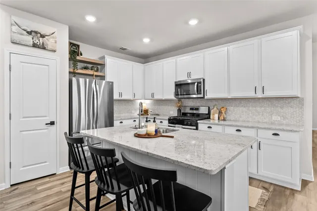 a kitchen with stainless steel appliances granite countertop a stove a refrigerator a sink a dining table and chairs with wooden floor