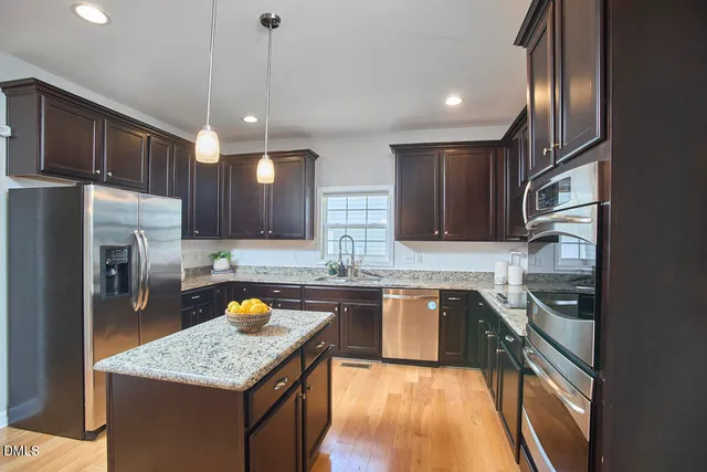 a kitchen with stainless steel appliances granite countertop a stove a refrigerator a sink a dining table and chairs with wooden floor