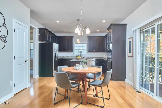 a kitchen with stainless steel appliances granite countertop a dining table chairs refrigerator and sink