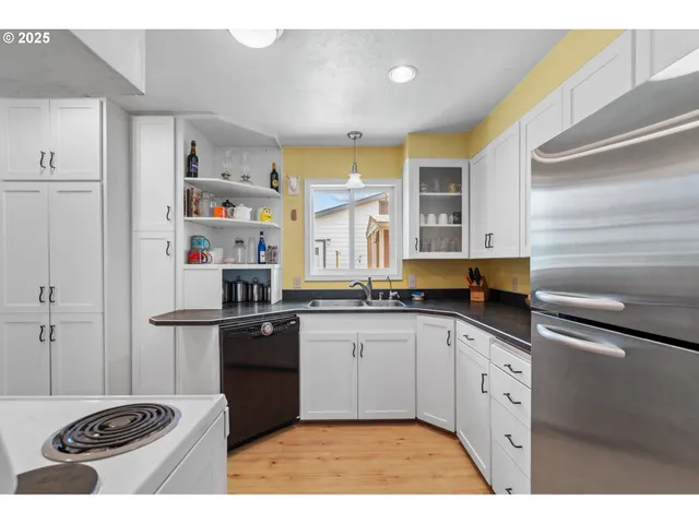 a kitchen with stainless steel appliances granite countertop a stove a refrigerator a sink dishwasher and white cabinets with wooden floor