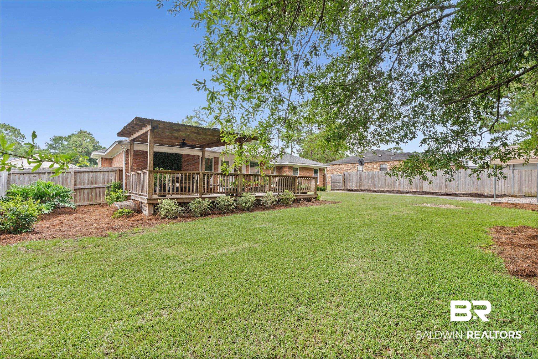 6501 Gas Light Lane South Mobile, AL 36695 - Photo 21 of 23 Spacious backyard featuring a manicured lawn, a raised wooden deck with a pergola, and mature trees providing natural shade