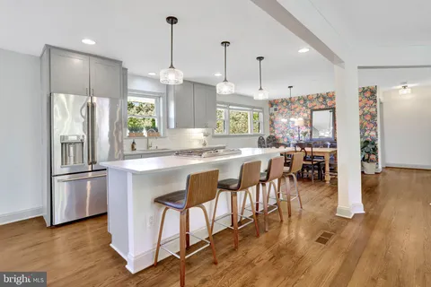 a kitchen with stainless steel appliances granite countertop a refrigerator a sink dishwasher a stove and a dining table with wooden floor