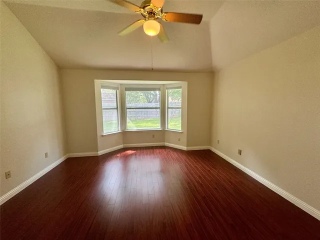an empty room with wooden floor fan and windows