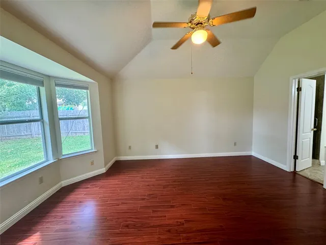 an empty room with wooden floor fan and windows