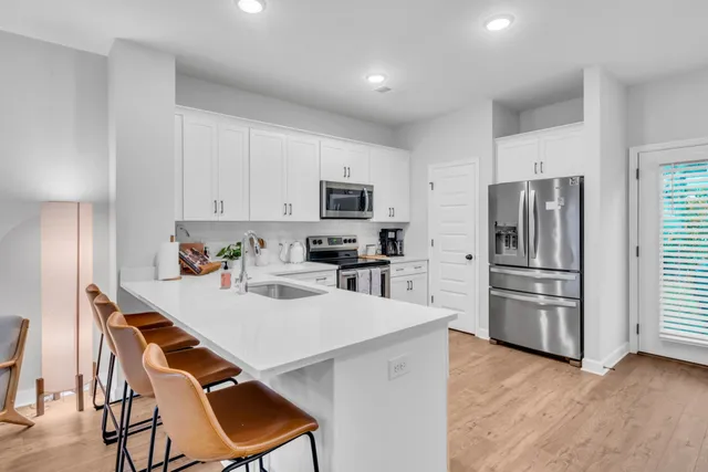 a kitchen with stainless steel appliances a refrigerator a stove a dining table and chairs with wooden floor