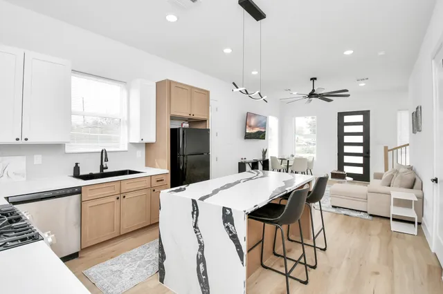 a kitchen with stainless steel appliances kitchen island granite countertop a refrigerator a sink dishwasher a dining table and chairs with wooden floor