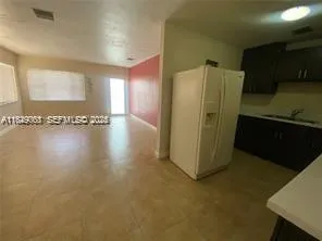 a view of a refrigerator in kitchen and an empty room