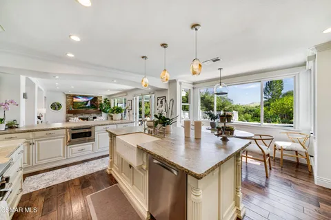 a kitchen with kitchen island granite countertop a stove a sink a refrigerator and white cabinets with wooden floor