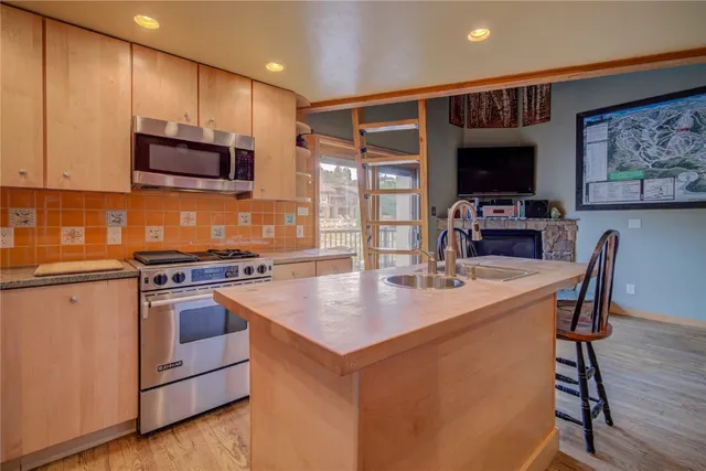 a kitchen with stainless steel appliances granite countertop a stove top oven a sink a dining table and chairs with wooden floor