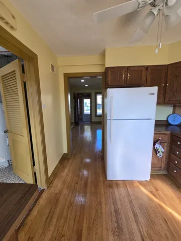 a view of a refrigerator in kitchen and an empty room with wooden floor