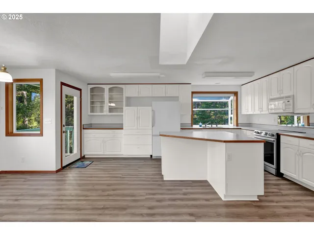 a kitchen with stainless steel appliances granite countertop a refrigerator a sink dishwasher a stove and white countertops with wooden floor