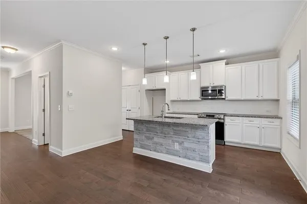 a large kitchen with granite countertop a stove a sink a refrigerator and white cabinets with wooden floor