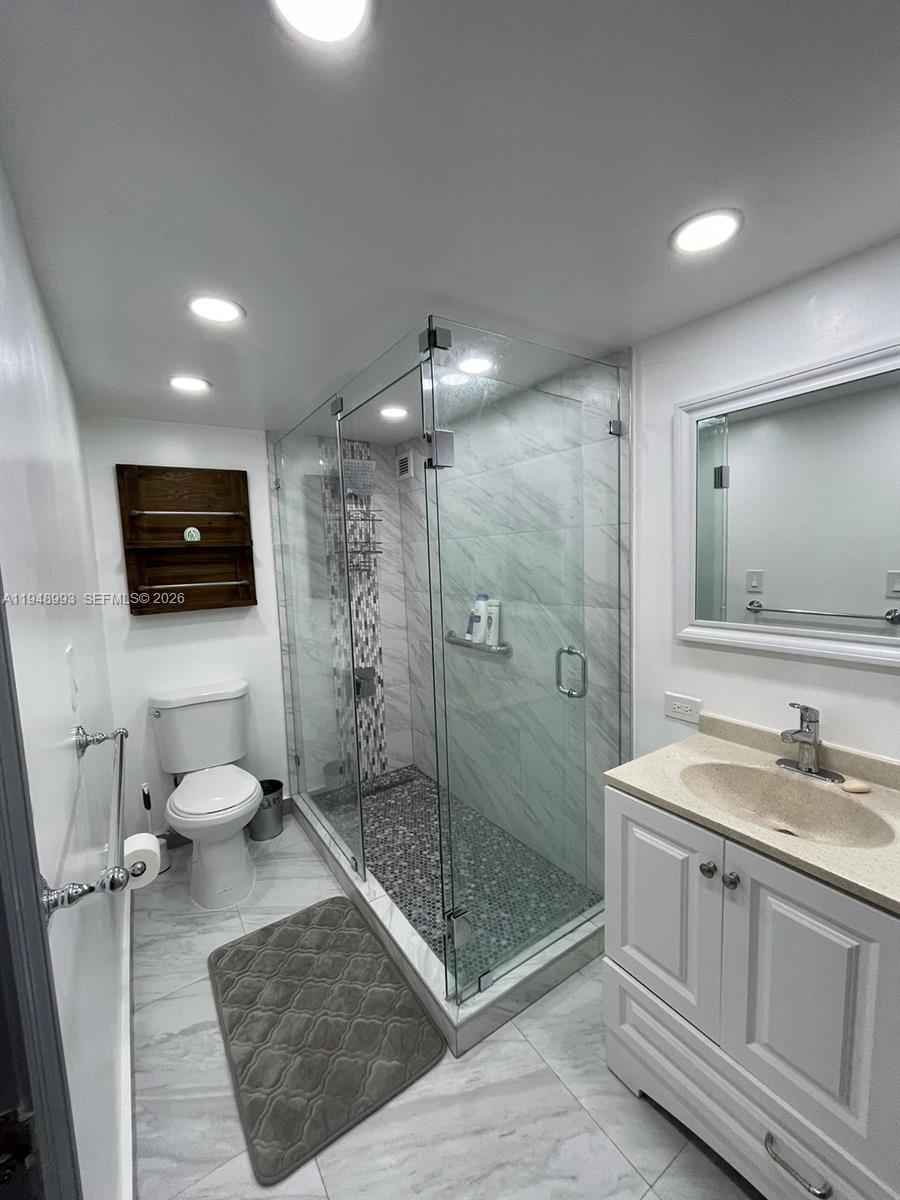 16919 North Bay Road, Unit 104 Sunny Isles Beach, FL 33160 - Photo 15 of 32 a bathroom with a granite countertop sink a toilet a mirror and shower