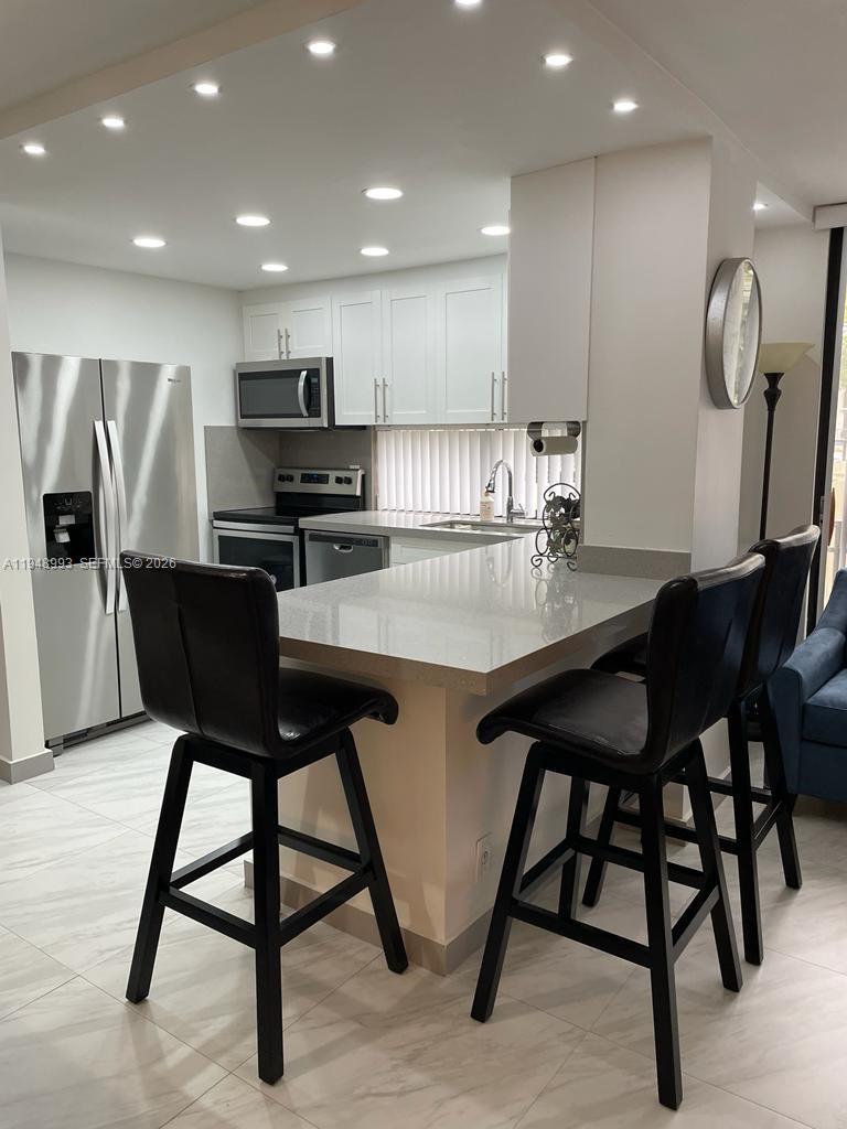 16919 North Bay Road, Unit 104 Sunny Isles Beach, FL 33160 - Photo 6 of 32 a kitchen with stainless steel appliances kitchen island granite countertop a table chairs refrigerator and microwave