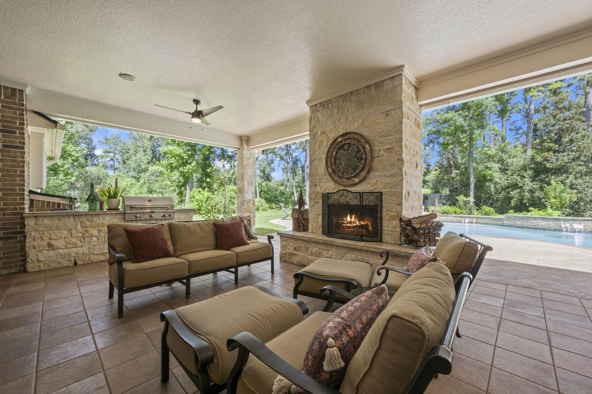 4106 Angling Lane Spring, TX 77386 - Photo 13 of 50 Experience outdoor luxury with this spacious covered patio, featuring a cozy stone fireplace, comfortable seating, and a scenic view of the pool and lush greenery.