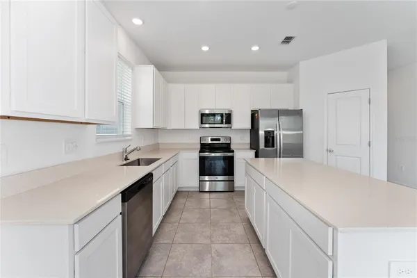 a large kitchen with a large counter top a sink stainless steel appliances and cabinets