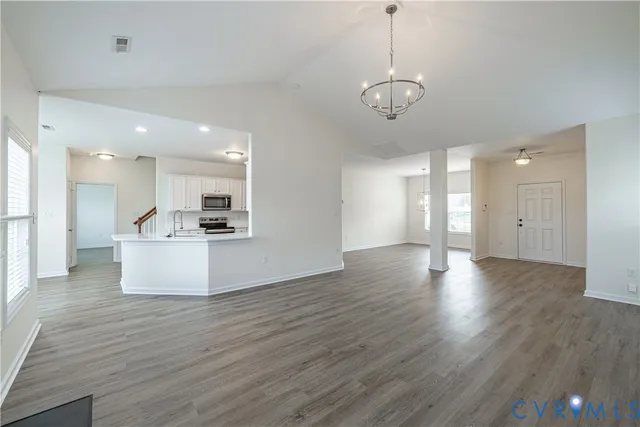 a view of an empty room and kitchen with wooden floor