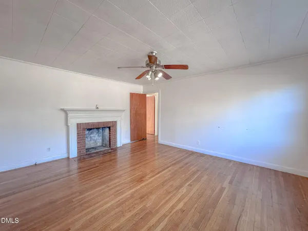 a view of an empty room with wooden floor and a fireplace